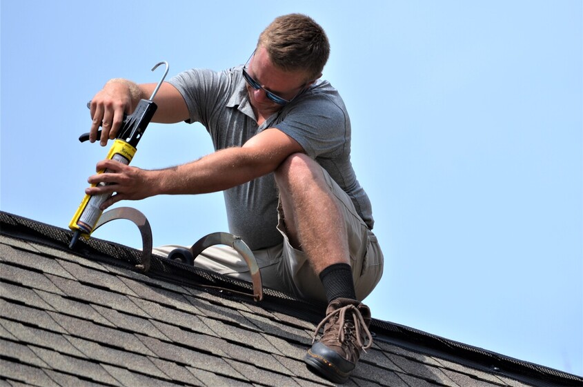 PICTURED HERE IS TYLER PHILLIPS FROM CWR OF OHIO SEALING OFF ONE OF THE BATS EXIT POINTS IN THE ROOF WITH CAULK