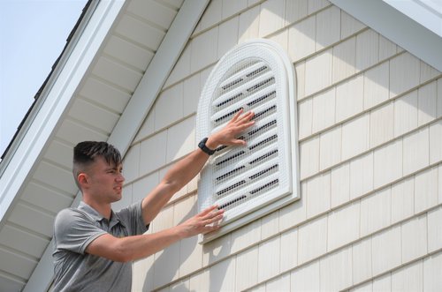  USING WIRE MESH TO GUARD AN ATTIC GABLE VENT TO PREVENT CAVITY NESTING BIRDS - June 7, 2021 - Pictured here is Alex Svensen fastening white wire mesh to a gable vent on a house in Ohio to prevent English house sparrows and European starlings from getting inside to nest. If you are looking for bird removal services near you, contact CRW at 440-236-8114 to hire a professional bird control company to get birds out of your attic, chimney, dryer vent, garage, roof, house, gutters, walls, garden, loft, basement, backyard and soffits.